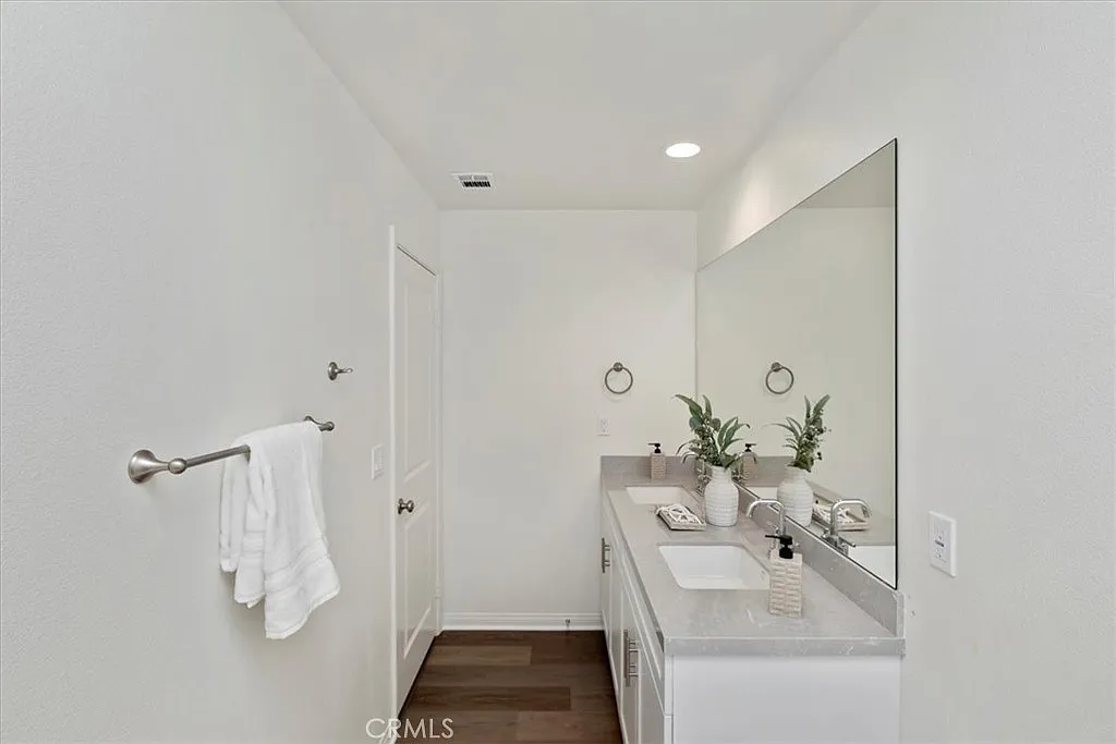 bathroom with large mirror, light-colored walls, countertop with plants and toiletries, and towel rack.