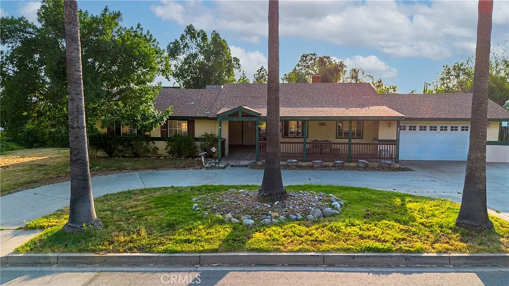 Large single-story house real estate with porch, trees, yard, and side garage.