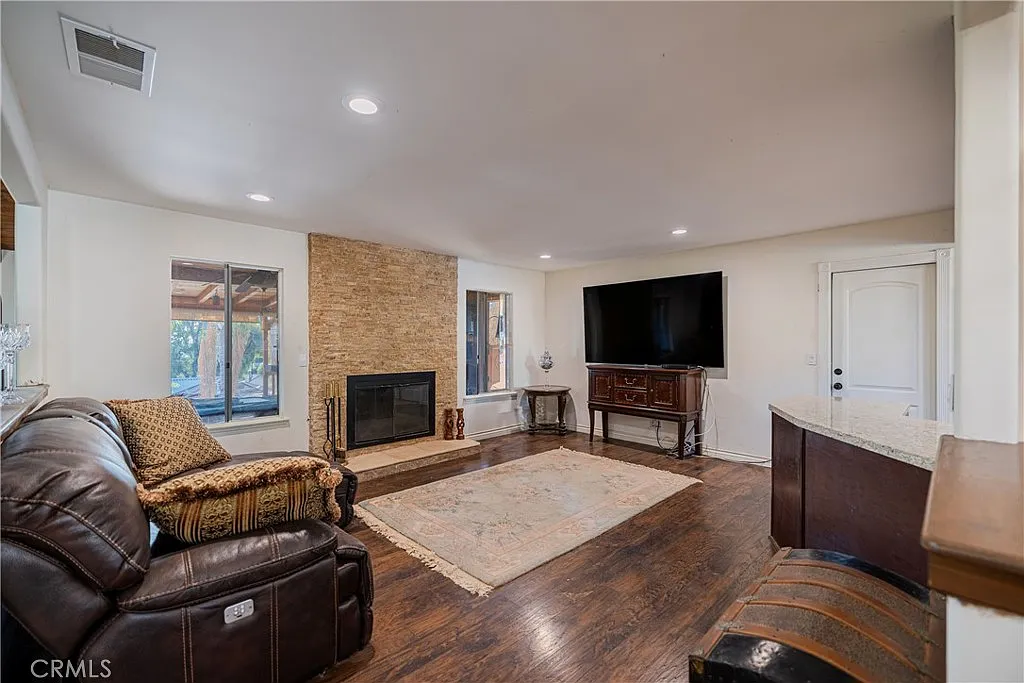 Living room with flat-screen tv, stone fireplace, dark wood floor, leather couch, decorative furniture