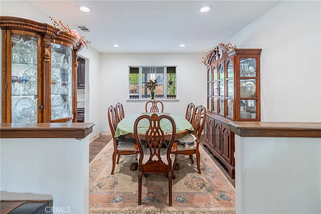 Dining room with wooden table, six chairs, area rug, two cabinets, and natural light from window.