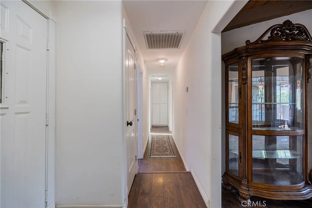 Hallway with white walls, wooden floor, and glass display cabinet on the right side.