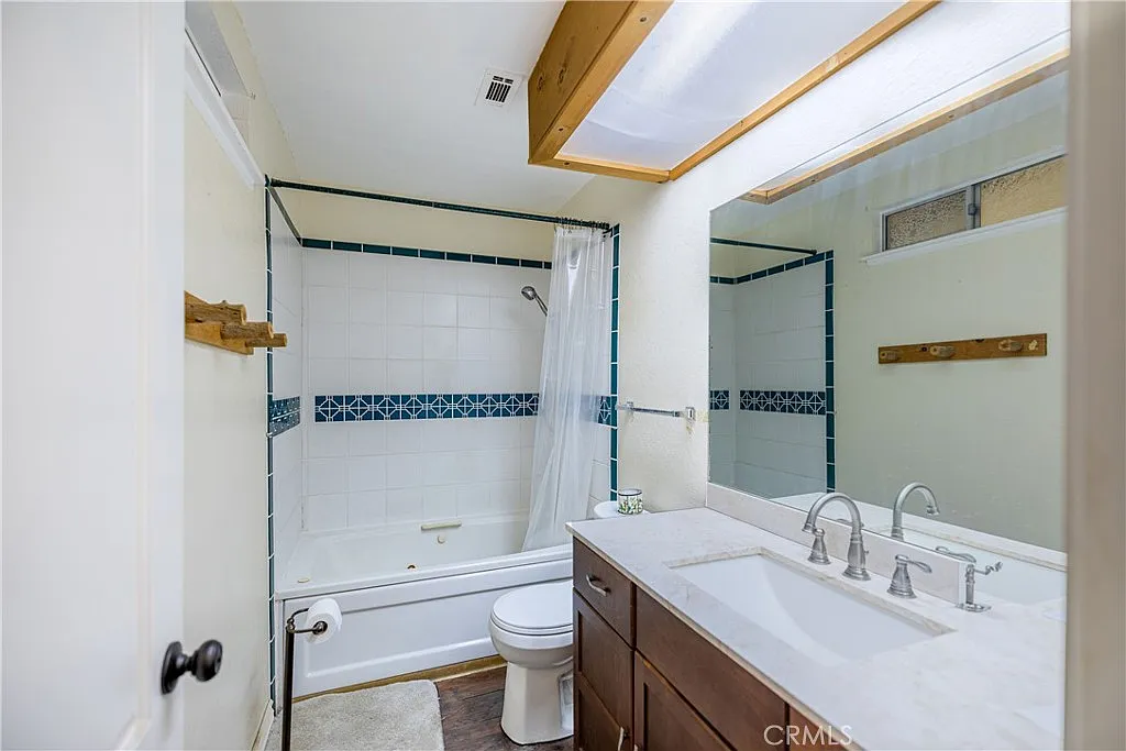 Bathroom with shower-tub combo, white walls, wooden beam ceiling, double-sink vanity with dark wood cabinets, and large mirror.