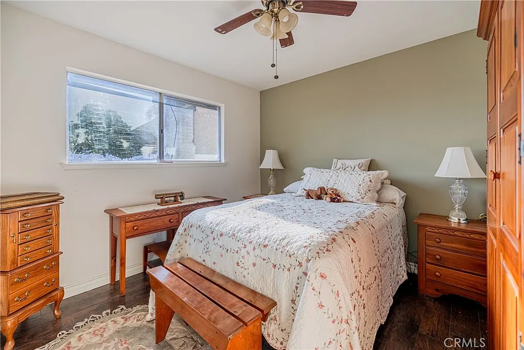 Bedroom with bed, floral bedding, green wall, bedside lamps, wooden nightstand, bench, and large window