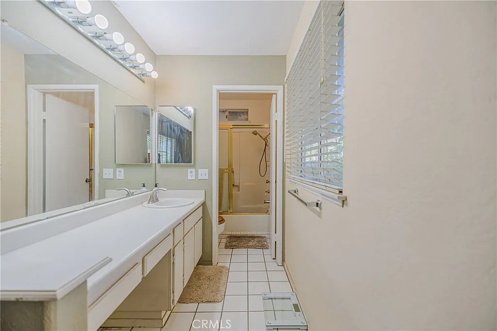 Bathroom with dual sinks, large mirror, light fixtures, shower stall, and white tile floor.