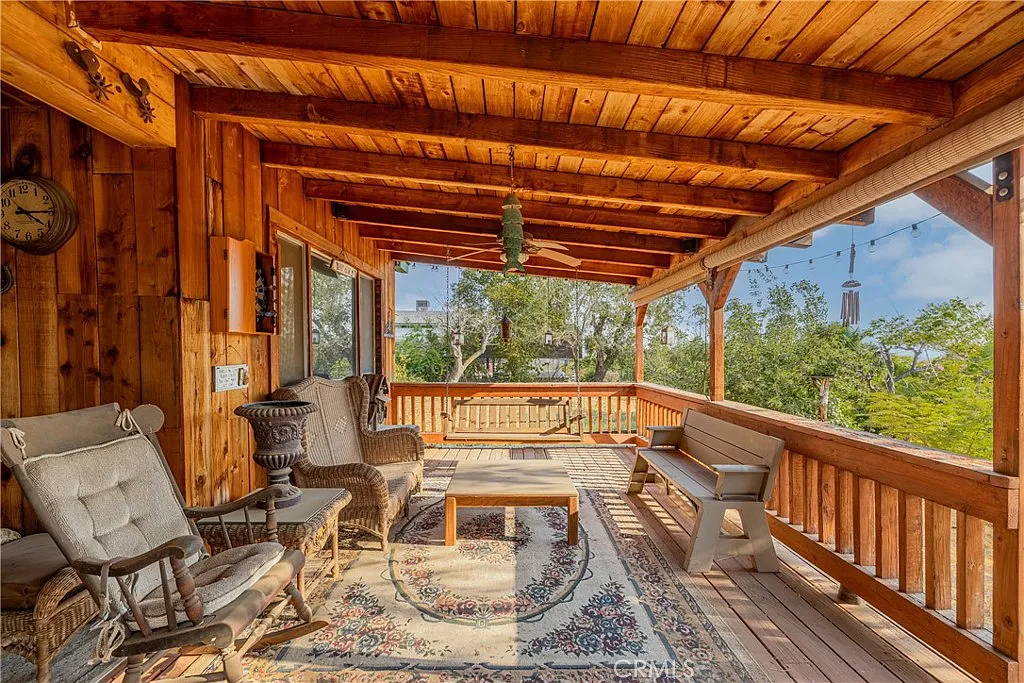 Wood porch with seating, table, decor, large windows, and greenery.