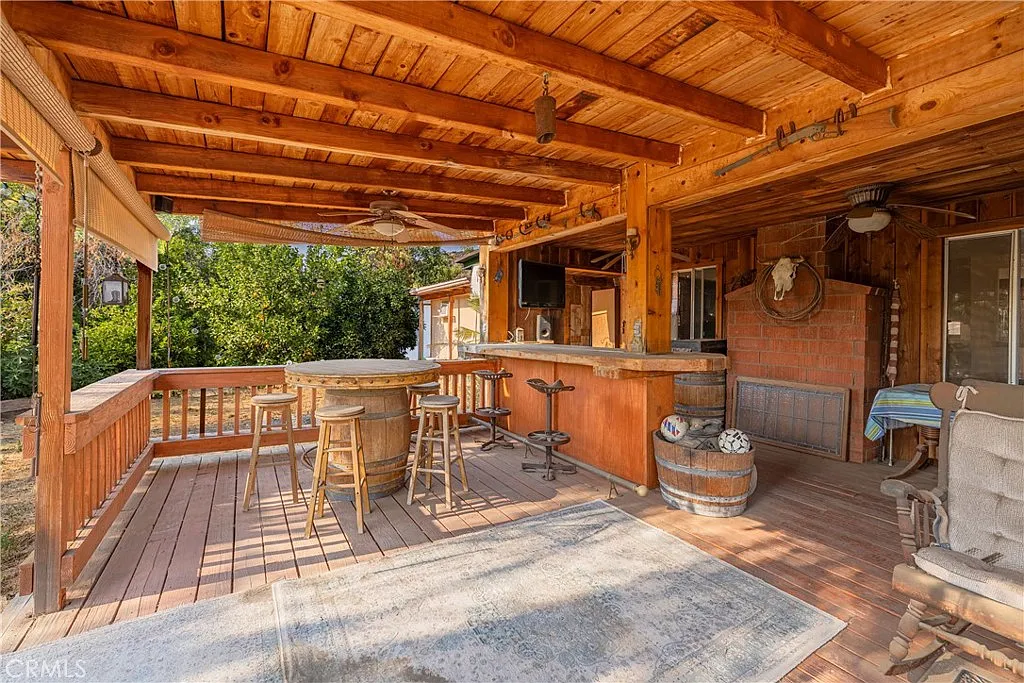 Wooden patio with bar area, stools, rustic design, and surrounding trees.