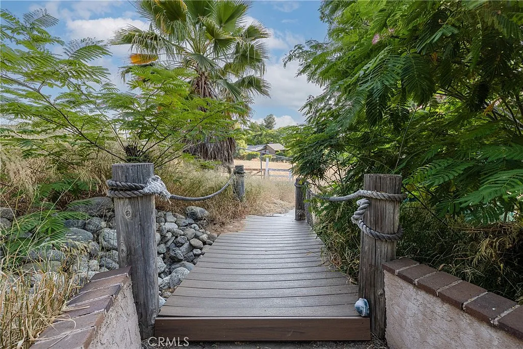 Wooden pathway with posts and ropes leading through greenery.