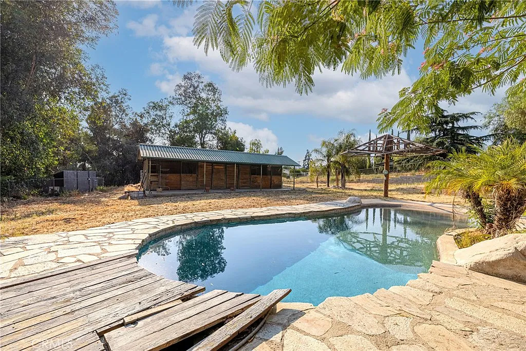 Swimming pool with stone patio, grassy area, trees, and barn nearby, California real estate.