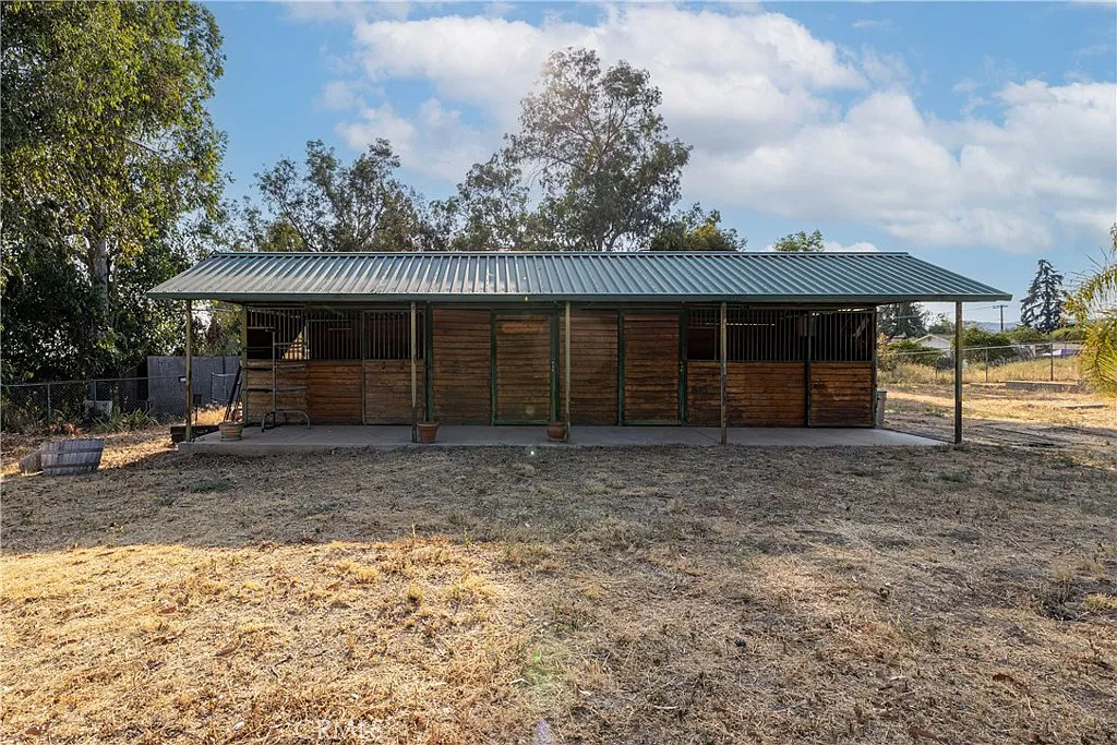 Barn with green metal roof, stalls, grass, and surrounding trees.