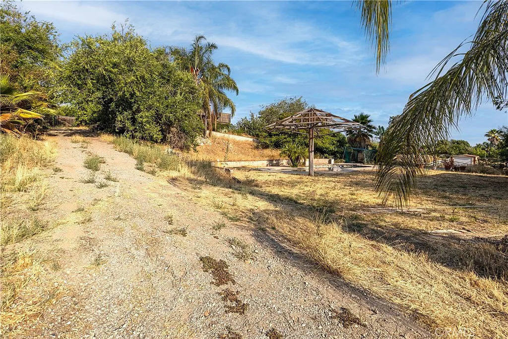 Dirt path through dry grass with trees and old structure in the background.