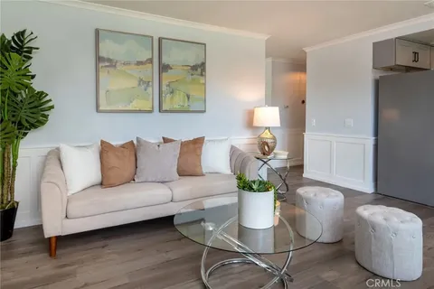 living room with light sofa, decorative pillows, glass coffee table, two round stools, framed artworks, and potted plant in corner