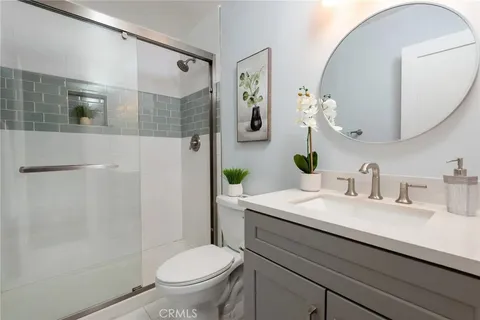 Bathroom with glass shower, gray cabinets, round mirror, and plants and artwork