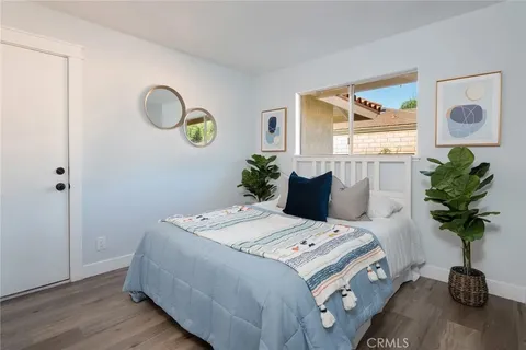 Bedroom with bed, light blue blanket, decorative pillows, two potted plants, framed artworks, and round modern mirrors