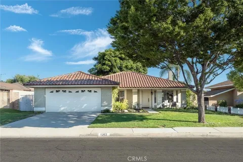 Single-story house real estate with tile roof, two-car garage, lawn, and trees.