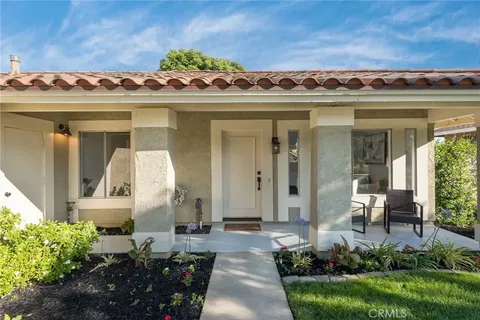 Front view of single-story real estate house with tiled roof, large windows, porch, and landscaped garden