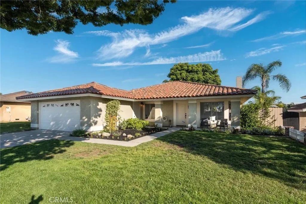 Single-story house real estate with brown tile roof, white walls, lawn, palms, and walkway.