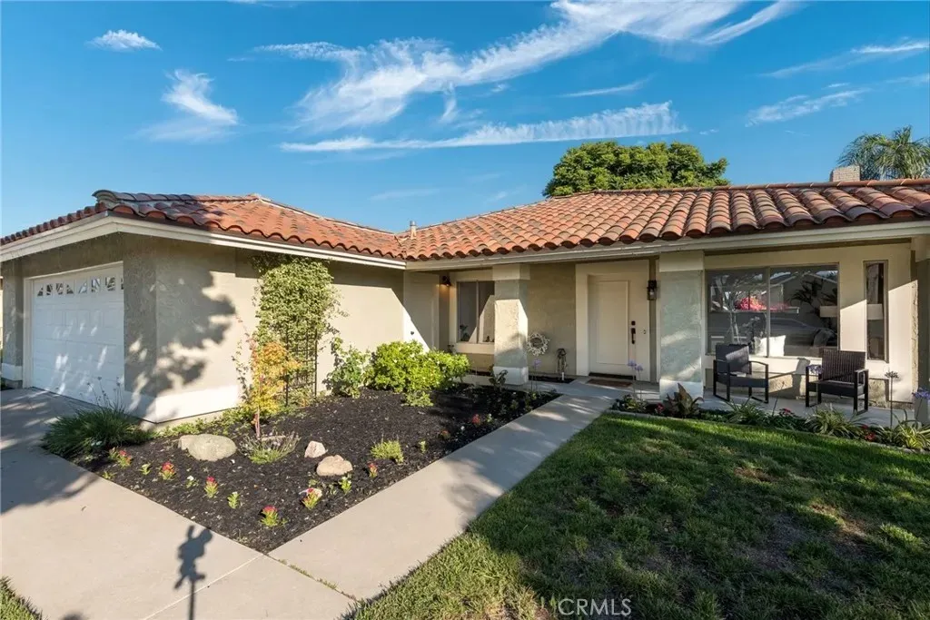 Single-story house real estate with tile roof, garden plants, pathway, and porch seating.