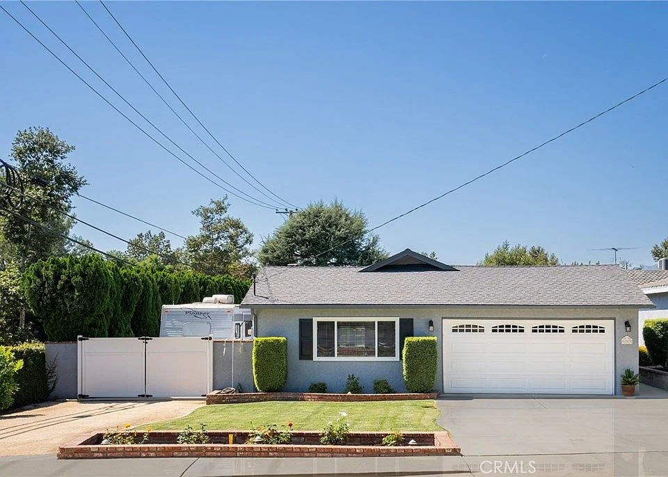 Single-story house California real estate with white garage door, bushes, and fence.