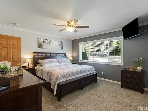 Bedroom with wooden bed, ceiling fan, window, dresser, and wall-mounted TV