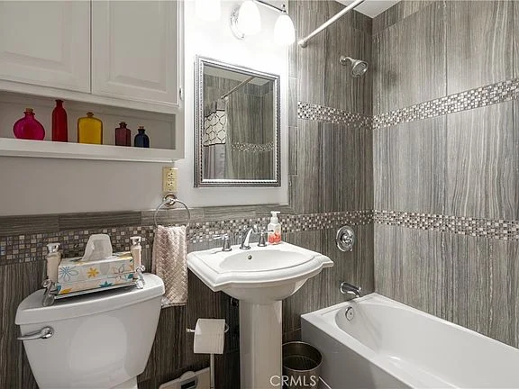 Bathroom with white sink, toilet, bathtub, gray tiles, mosaic strip, and mirror