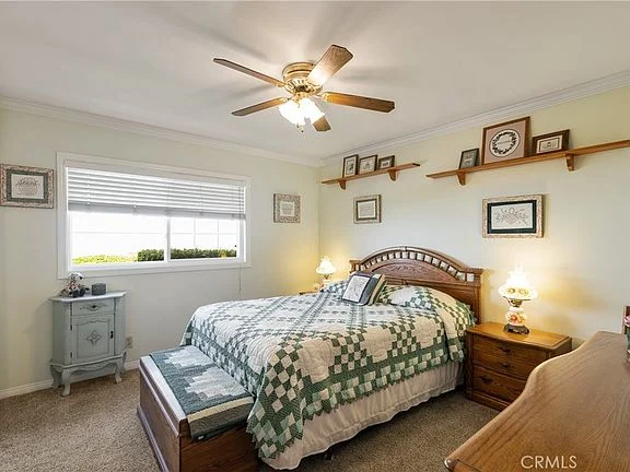 Bedroom with wooden bed, green and white quilt, bedside tables, dresser, and wall pictures