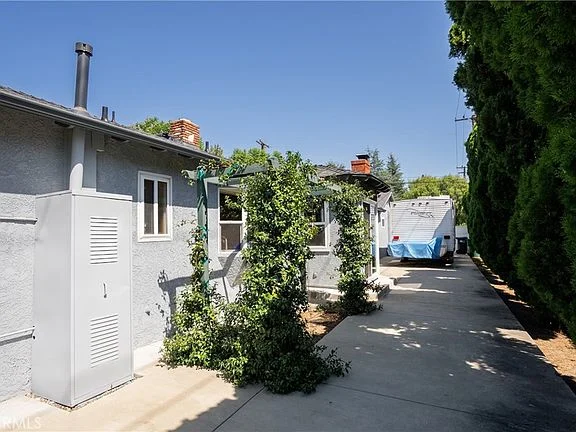 Narrow pathway beside California real estate house with greenery, shed, and trailer