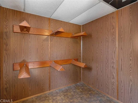 Room with wood-paneled walls, wall shelves, and textured floor