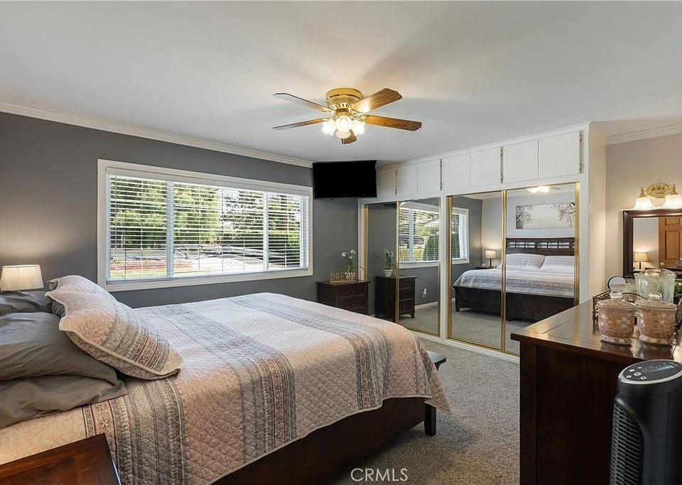 Bedroom with large bed, ceiling fan, windows, mirrored closets, and dresser