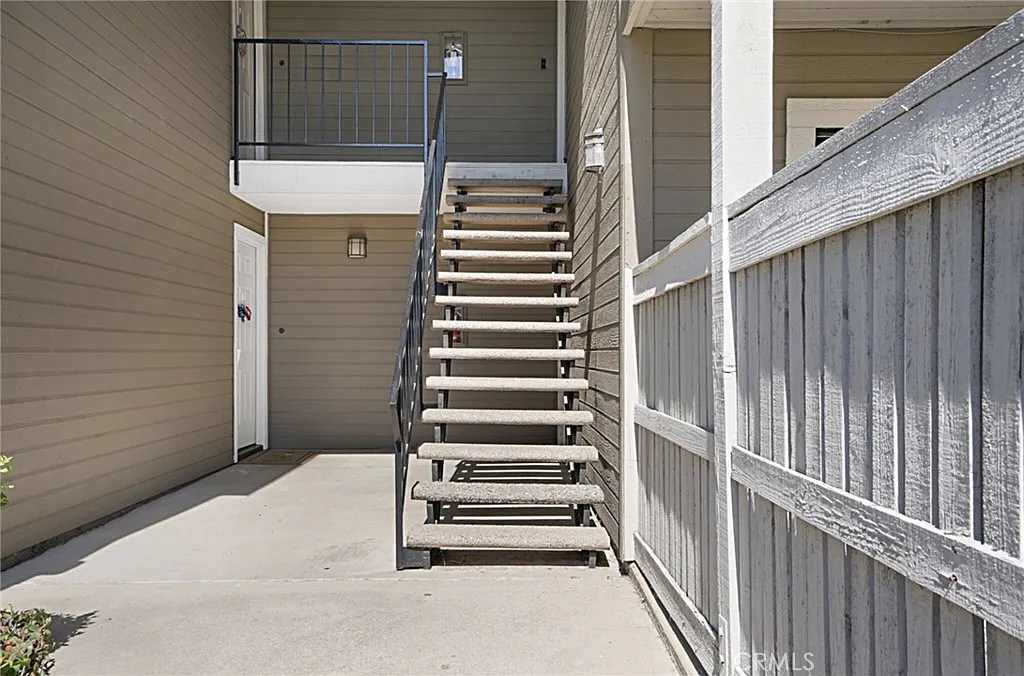 Metal stairs leading to upper level next to wooden fence and door under small overhang.