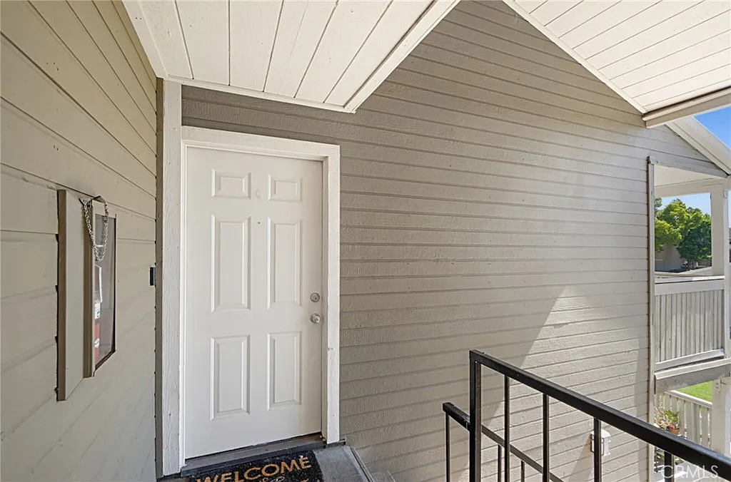 House entrance real estate with white door, gray siding, railing, and welcome mat.