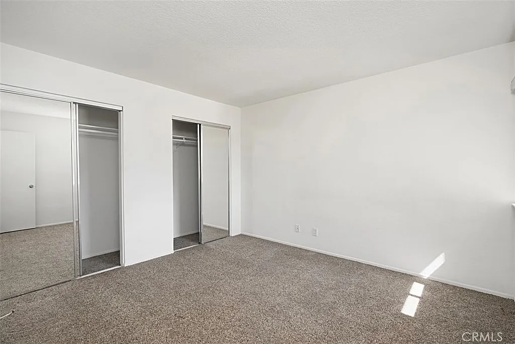 Empty room with light walls, carpeted floor, and two sliding closet doors.