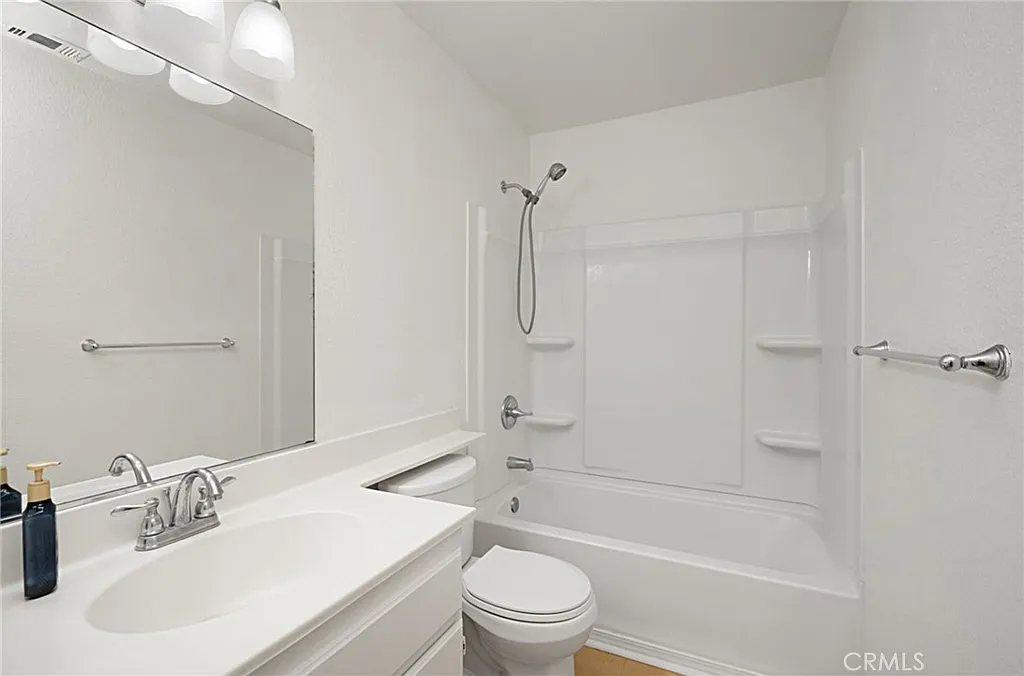 Bathroom with white bathtub and shower, large mirror above sink, and light-colored walls.