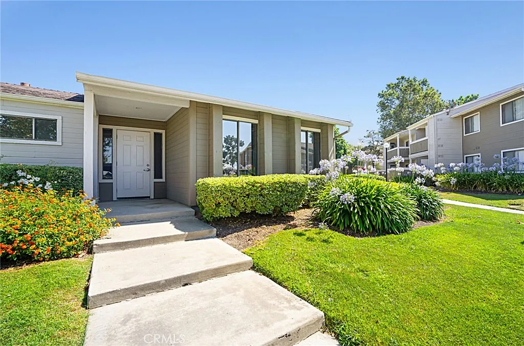 House real estate with front yard, shrubs, flower beds, and blue sky.