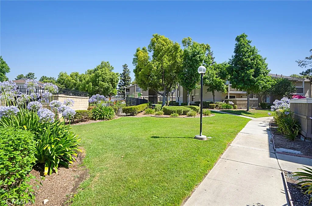 Landscaped garden path with green grass, trees, and flowering plants in residential area.