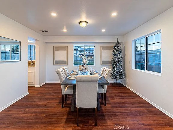 Dining room with table, chairs, large windows, Christmas tree, wooden floor, and white walls