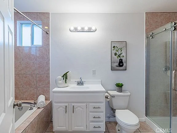 bathroom with white vanity, sink, toilet, pink tiles, glass shower, and bathtub