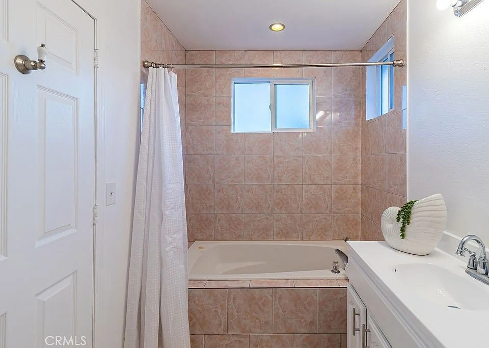 Bathroom with bathtub, shower curtain, window, light-colored tiles, and sink with decorative shell