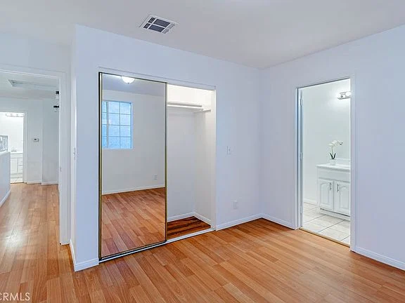 Bright room with white walls, hardwood floor, mirrored closet, and adjoining bathroom
