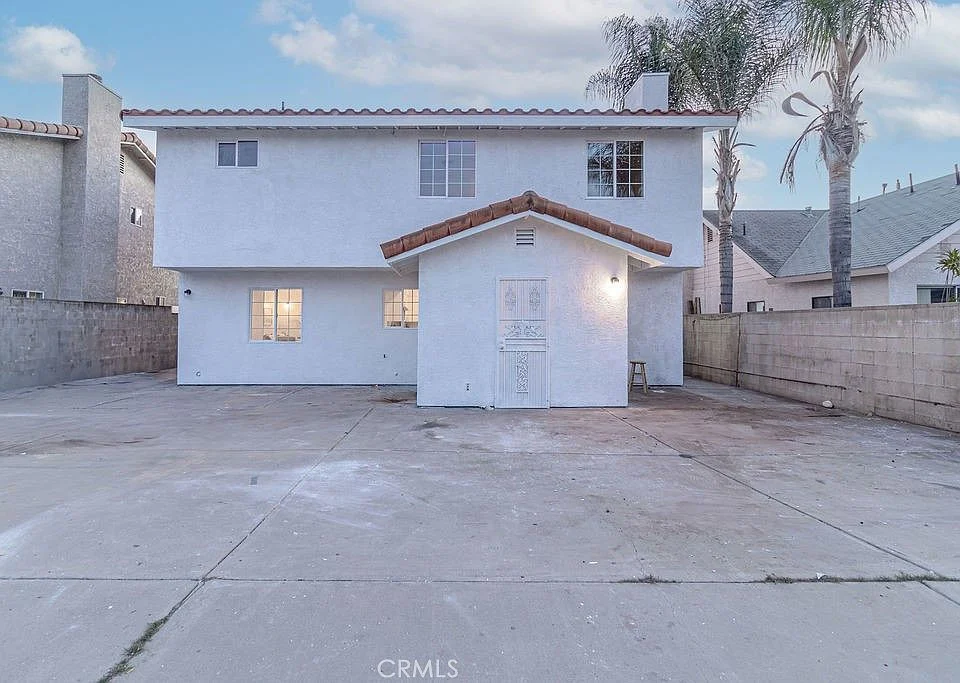 Two-story California real estate house with red tile roof, concrete yard, and palm trees