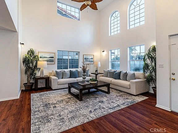 living room with two white sofas, decorative pillows, dark wooden coffee table, rug, plants, and wall art