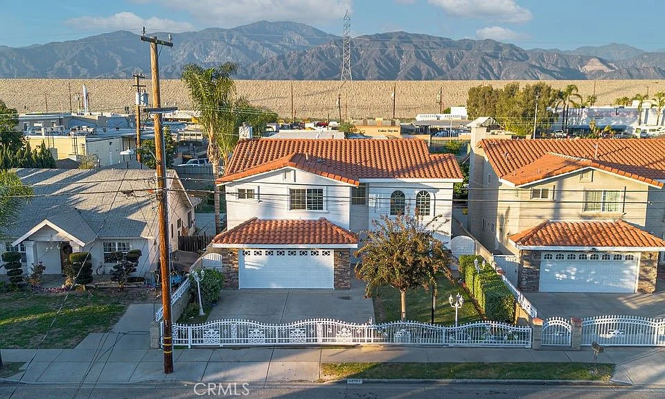 Aerial view of California real estate houses with tile roofs, mountains, and fence