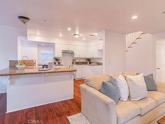 open-concept living space with kitchen, white cabinets, granite counter tops, hardwood floor, sofa, and staircase