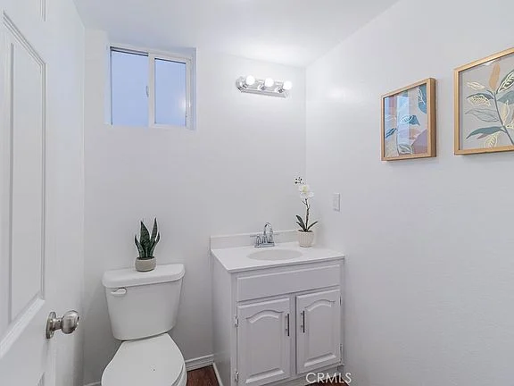 bathroom with white vanity, sink, toilet, window, plant prints, and potted plant