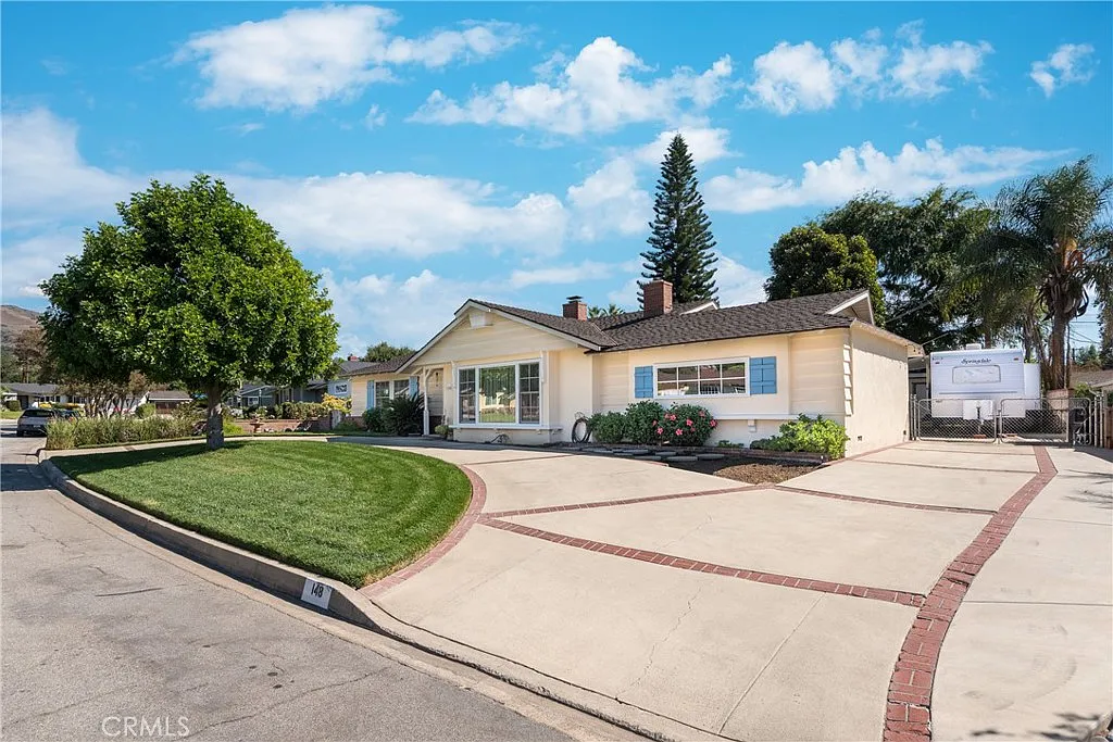 Luxury yellow single-story house with manicured lawn, driveway, and corner lot with trees, California real estate
