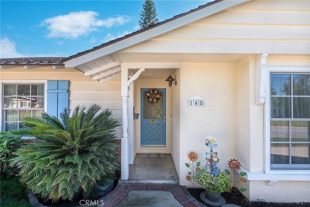Luxury yellow house with blue front door, wreath, and surrounding greenery, California real estate