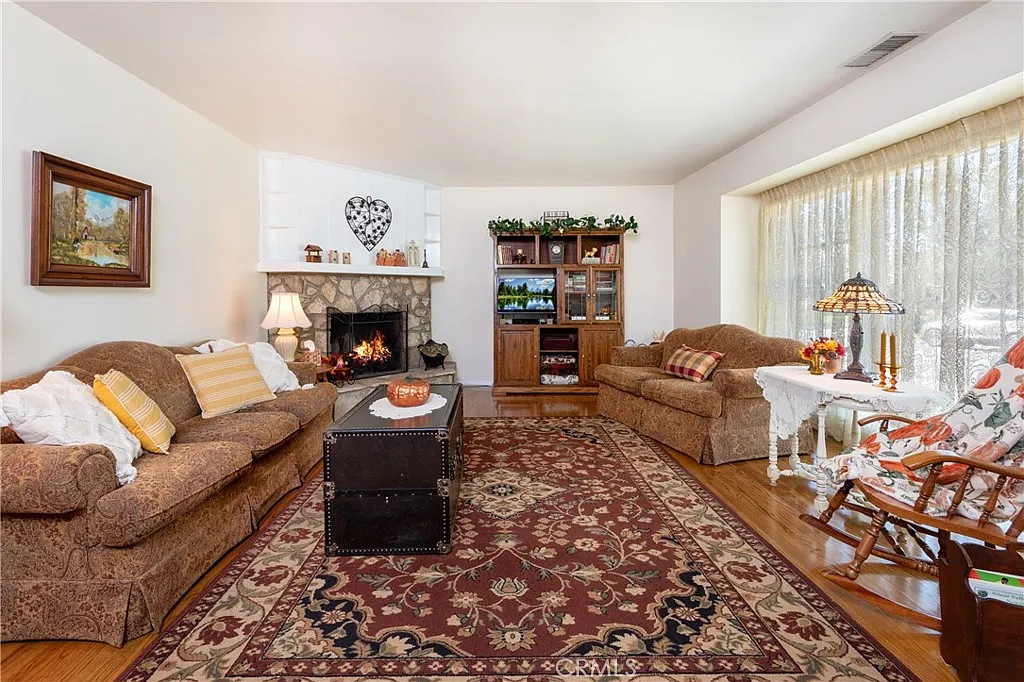 living room with stone fireplace, patterned sofas, wooden bookshelf, and colorful rug