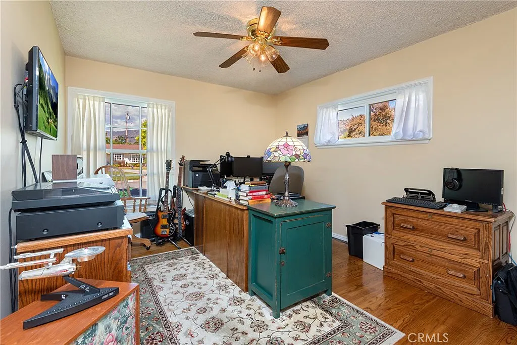 Home office with wooden desk, printer, electronics, guitar, and area rug