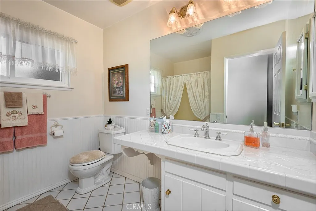 Bathroom with white sink, toilet, mirrors, light fixtures, and shower curtain