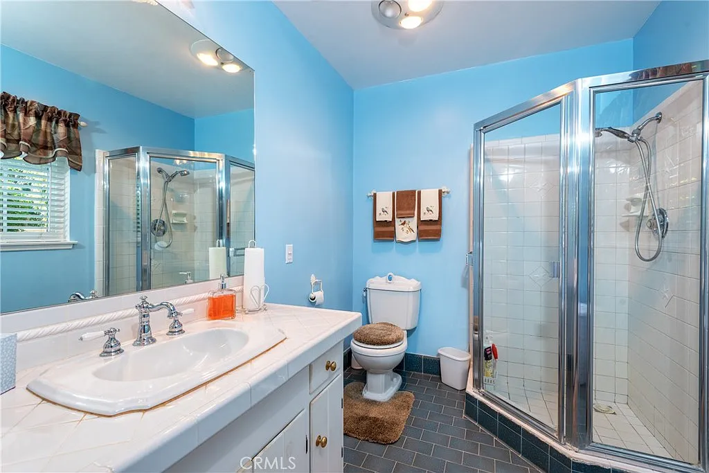 Bathroom with blue walls, glass shower, white toilet, double sink vanity, and towels