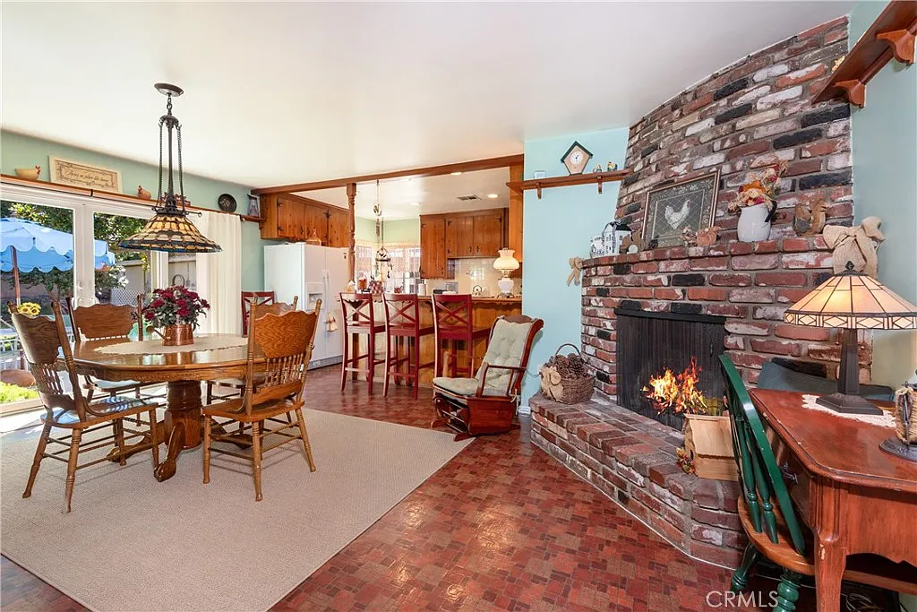 dining area with wooden table, chairs, brick fireplace, and kitchen with wooden cabinets in background
